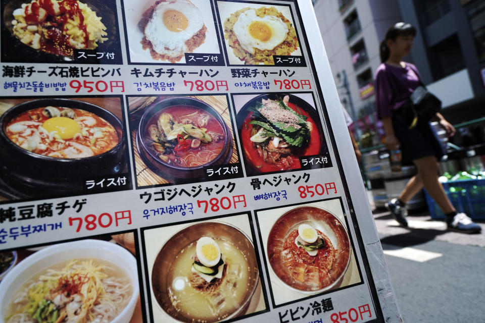 In this Aug. 13, 2019, photo, a woman walks past a menu of South Korean restaurant in Shin Okubo area in Tokyo. Tokyo’s Shin Okubo district bustles with Korean restaurants and stores selling K-pop merchandise. (AP Photo/Eugene Hoshiko)