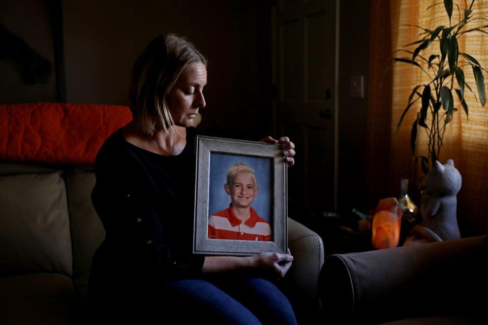 A woman sits on a couch in a darkened room, looking at a framed picture of a boy