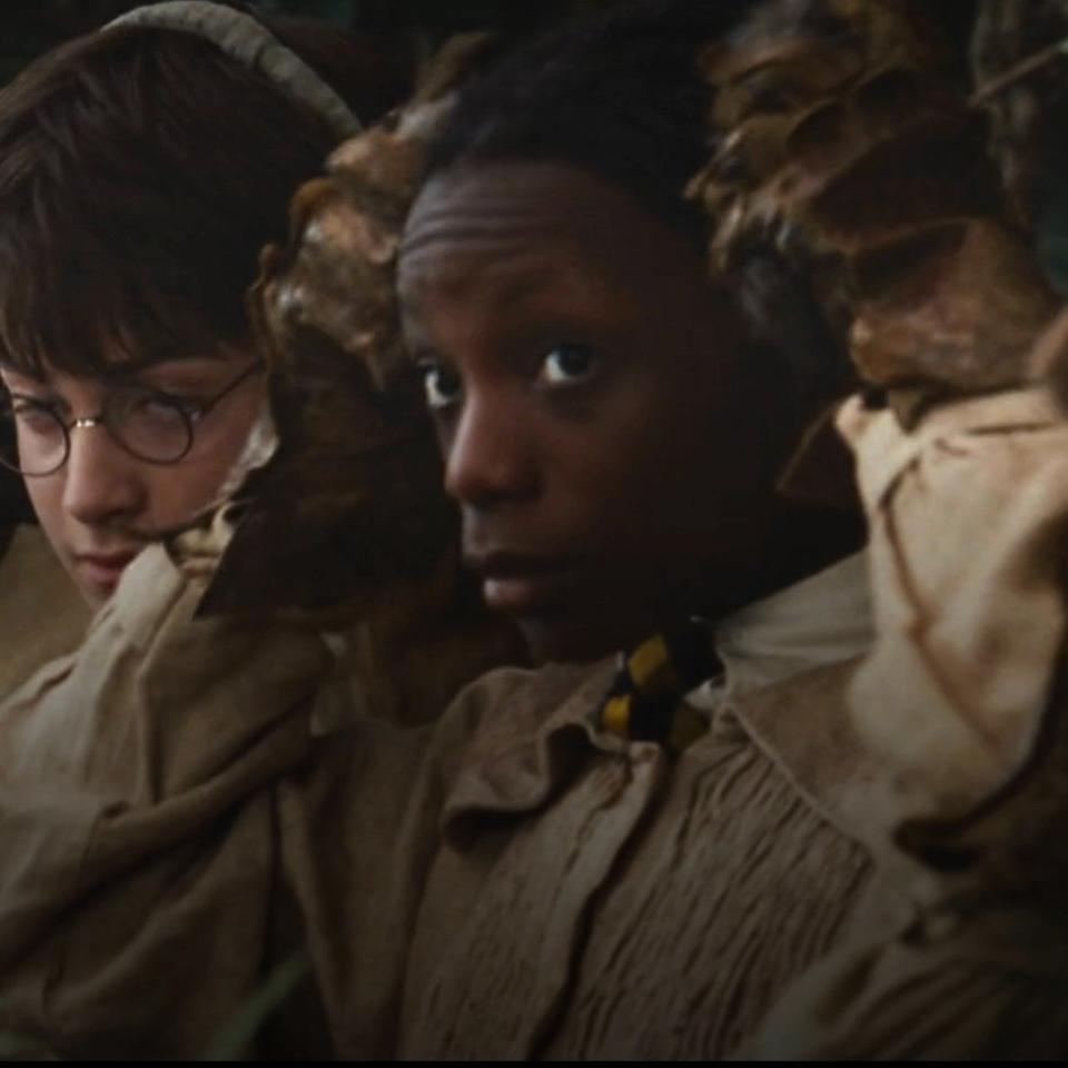 Harry Potter and classmate tend to plants while wearing earmuffs in a scene from a Harry Potter film