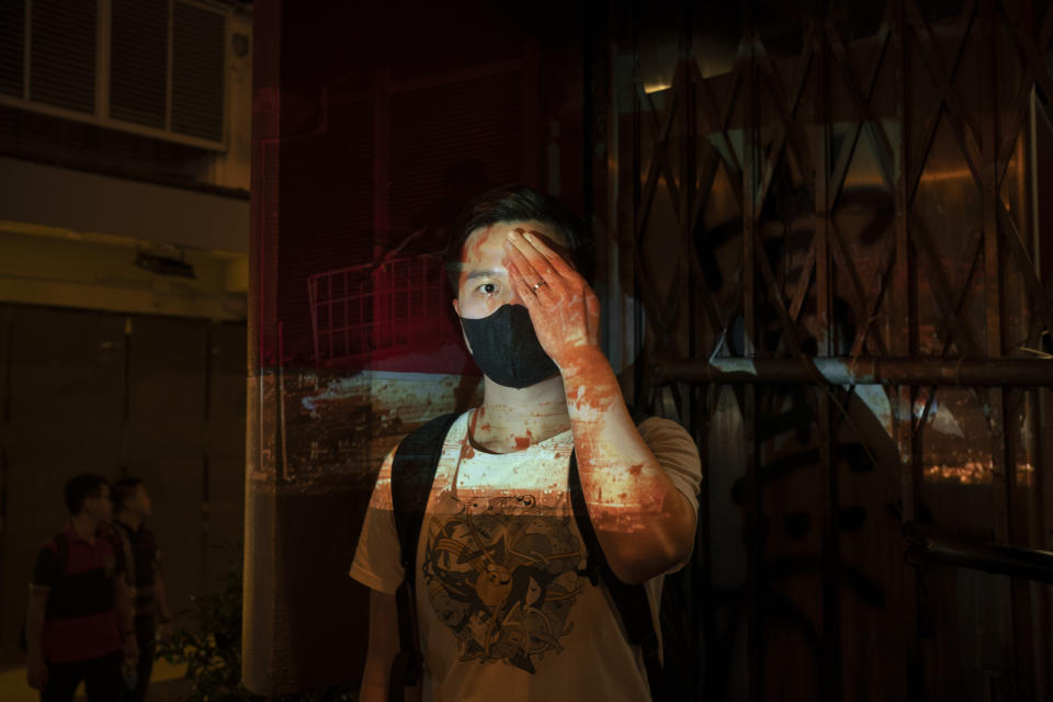 In this Oct. 20, 2019, photo, a protester who identified himself as Tom, poses for a portrait next to a damaged subway station as a projector displays a photograph, previously taken during the unrest, over him at a protest in Hong Kong. Tom said "If we don't wear the mask, the police can recognize you and say you are a rioter and arrest you for no reason, even if you are peacefully protesting. That's the white terror they want to do." (AP Photo/Felipe Dana)