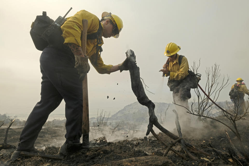 County of Santa Barbara Fire Department firefighters extinguish a roadside fire off the U.S. 101 highway Wednesday, Oct. 13, 2021, in Goleta, Calif. A wildfire raging through Southern California coastal mountains threatened ranches and rural homes and kept a major highway shut down Wednesday as the fire-scarred state faced a new round of dry winds that raise risk of flames. (AP Photo/Ringo H.W. Chiu)