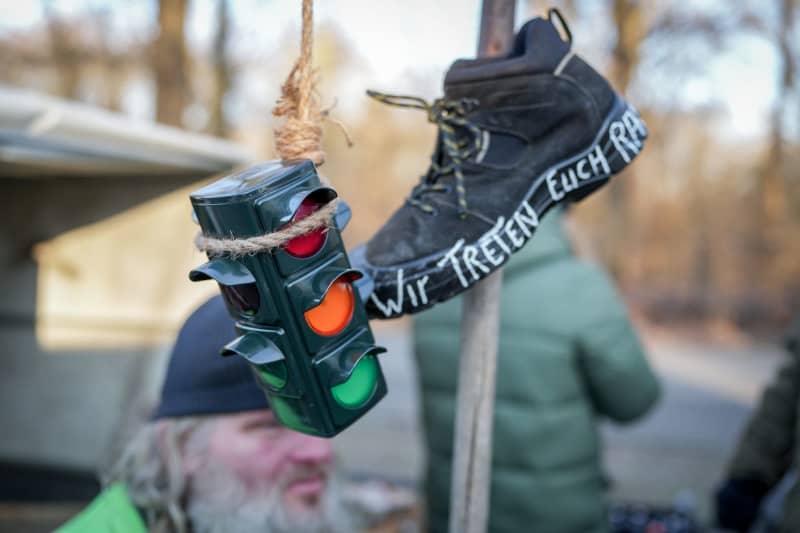 Farmers and craftsmen talk behind a symbolic traffic light and a shoe with the inscription "We'll kick you out" on the fringes of the farmers' protests in front of the Brandenburg Gate. In response to the federal government's austerity plans, the farmers' association has called for a week of action with rallies and rallies starting on January 8. It is to culminate in a major demonstration in the capital on January 15. Kay Nietfeld/dpa