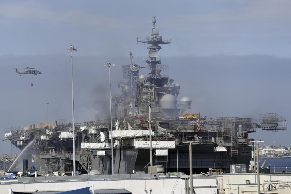 A helicopter carrying water passes the USS Bonhomme Richard, Tuesday, July 14, 2020, in San Diego. The battle to save the ship from a ravaging fire entered a third day in San Diego Bay on Tuesday with indications that the situation aboard the amphibious assault ship was improving. The U.S. Navy said in a statement late Monday that firefighters were making significant progress with the assistance of water drops by helicopters. (AP Photo/Gregory Bull)