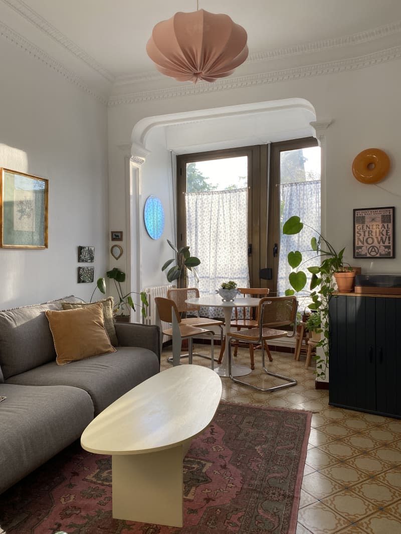 White living room with gray sofa, fabric-covered pendant lamp, and oval coffee table with view into dining room