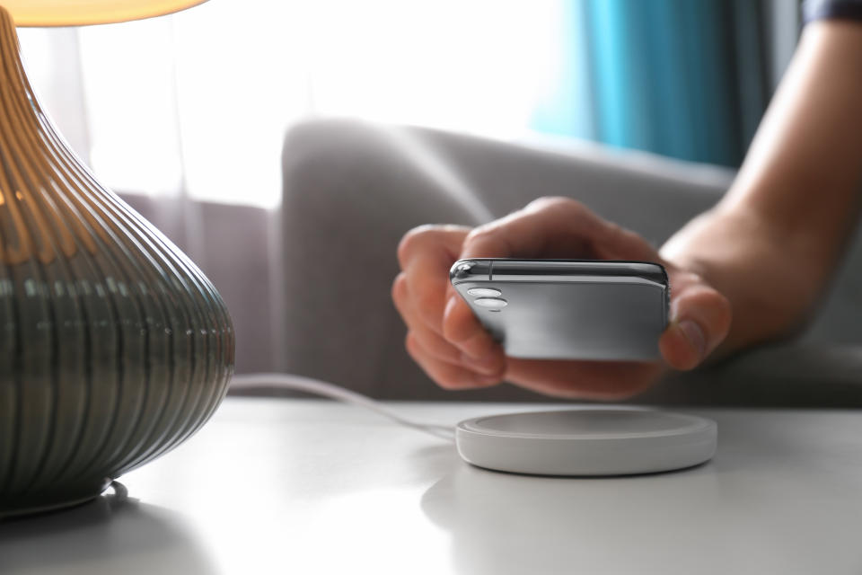 Man putting smartphone on wireless charger in room, closeup