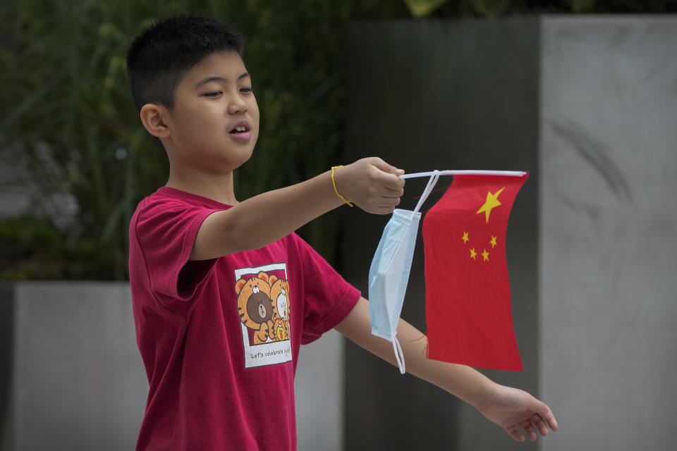 A kid hangs his face mask on a national flag as he walks on a street in Beijing, Tuesday, Aug. 9, 2022. Chinese authorities have closed Tibet's famed Potala Palace after a minor outbreak of COVID-19 was reported in the Himalayan region. (AP Photo/Andy Wong)