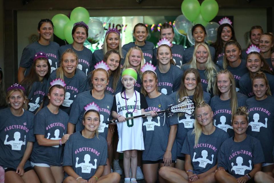 Lucy Donmoyer (center) was presented with a jersey and lacrosse stick before a March 2022 game by the Jacksonville University women's soccer team, which adopted Lucy through the Friends of Jaclyn, a foundation that matches children with serious pediatric illnesses with college and high school athletic teams.