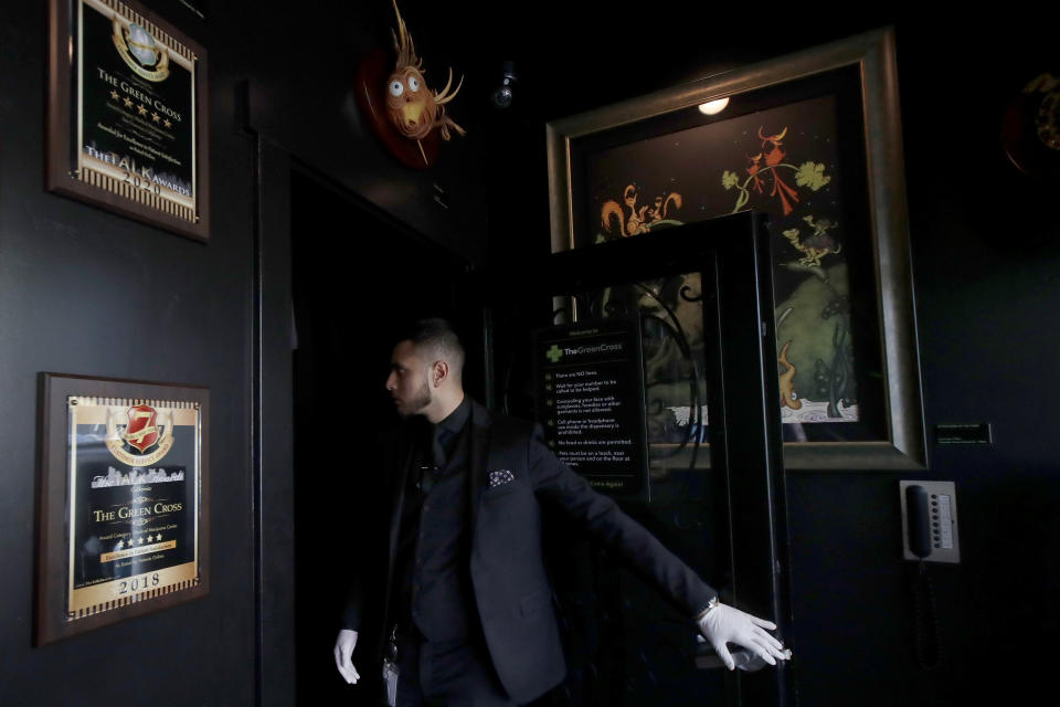 The Green Cross cannabis dispensary employee Ruben Arias watches the number of customers in the showroom in San Francisco, Wednesday, March 18, 2020. As about 7 million people in the San Francisco Bay Area are under shelter-in-place orders, only allowed to leave their homes for crucial needs in an attempt to slow virus spread, marijuana stores remain open and are being considered "essential services." (AP Photo/Jeff Chiu)