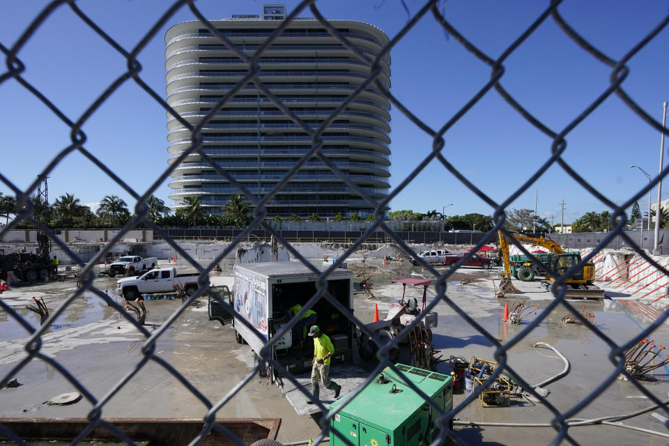 Workers pump water out of the foundation of the former Champlain Towers South building, Thursday, May 12, 2022, in Surfside, Fla. The Eighty Seven Park building is to the south. Parties associated with the building and others have agreed to a settlement of $997 million to compensate the victims and families of those killed when the Champlain Towers South building collapsed nearly a year ago. (AP Photo/Marta Lavandier)