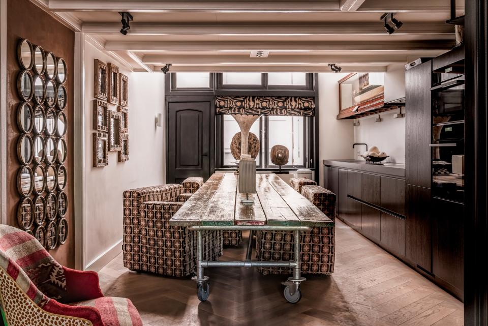 A long industrial table is surrounded by boxy club chairs, which are upholstered in a geometric pattern.