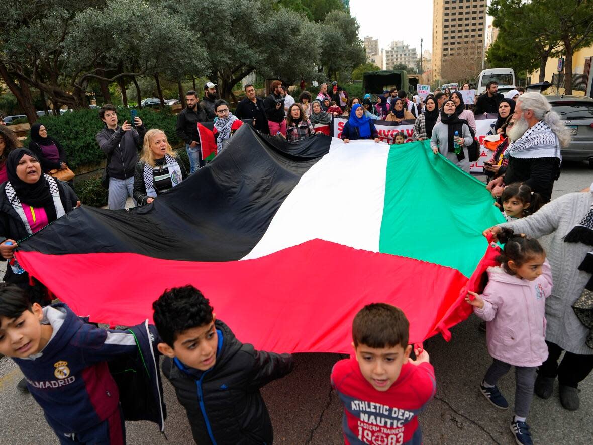 Activists and their children hold a giant Palestinian flag during a protest demanding that countries resume funding of the United Nations Relief and Works Agency for Palestinians Refugees (UNRWA) near the European Union headquarters in Beirut, Lebanon on Wednesday, Feb. 7, 2024. (Bilal Hussein/Associated Press - image credit)