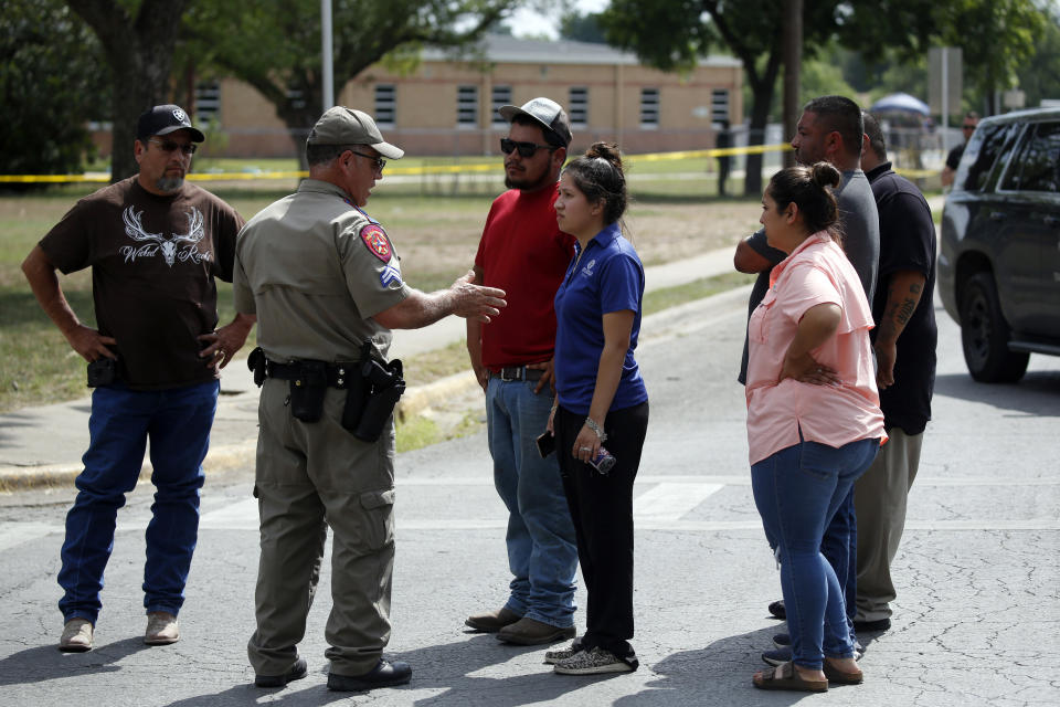 FILE - A policeman talks to people asking for information outside of the Robb Elementary School in Uvalde, Texas, Tuesday, May 24, 2022. A gunman fatally shot 19 children and two teachers at the school. Over an hour passed from the time officers followed the 18-year-old gunman into the school and when they finally entered the fourth grade classroom where he was holed up and killed him. Meanwhile, students trapped inside repeatedly called 911 and parents outside the school begged officers to go in. On July 17, 2022, a damning report on the response was released by an investigative committee from the Texas House of Representatives as well as hours of body camera footage, further laying bare the chaotic response that included 376 officers. (AP Photo/Dario Lopez-Mills, File)