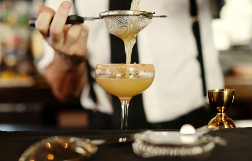 a bartender pours a freshly made drink into a glass