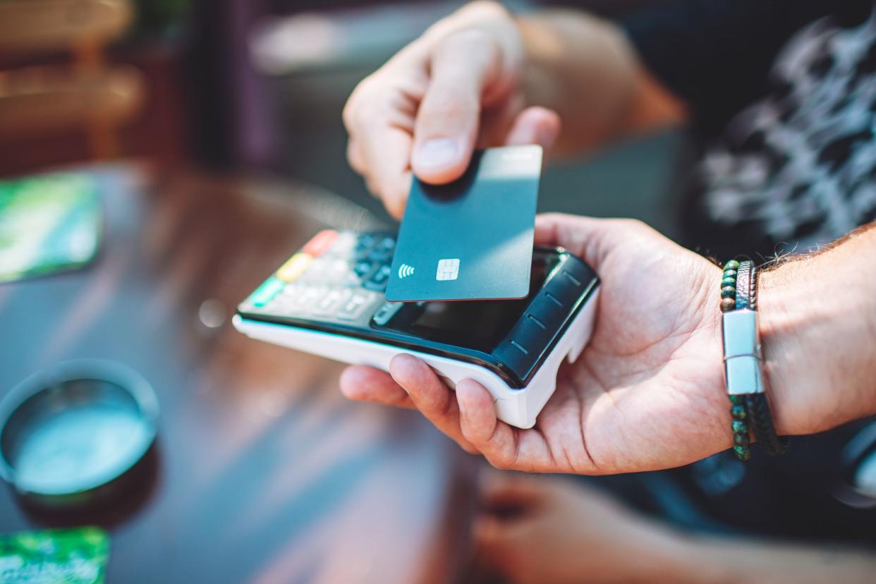 Adult man paying with credit card at cafe, close-up of hands with credit card and credit card reader