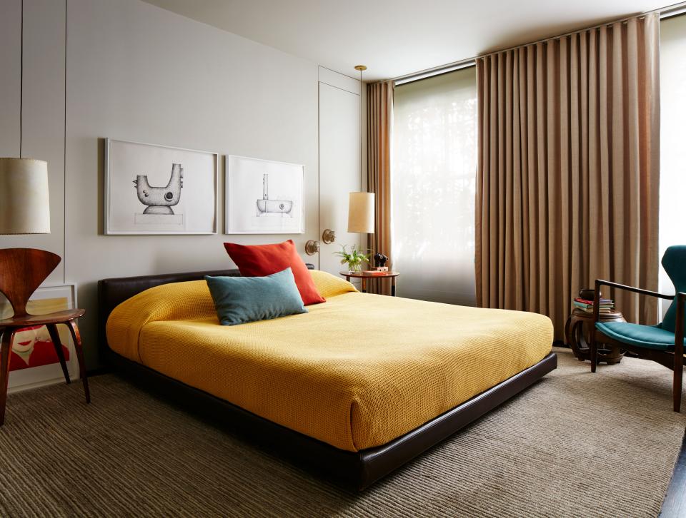 Drawings of some of Otero's early ceramic pieces hang above the master bed. While Otero added some historical splendor in the reception rooms—including moldings and architraves—he decided to keep bathrooms, kitchen, and his main bedroom more sleek and minimal. "I like an overall clean tone with consistency through spaces," he says. The rug is from Beauvais; the curtains are from Schumacher; the bedside pendant lamps are custom. The room's walls are painted in Benjamin Moore China White, while the saffron yellow coverlet is from Area Home.