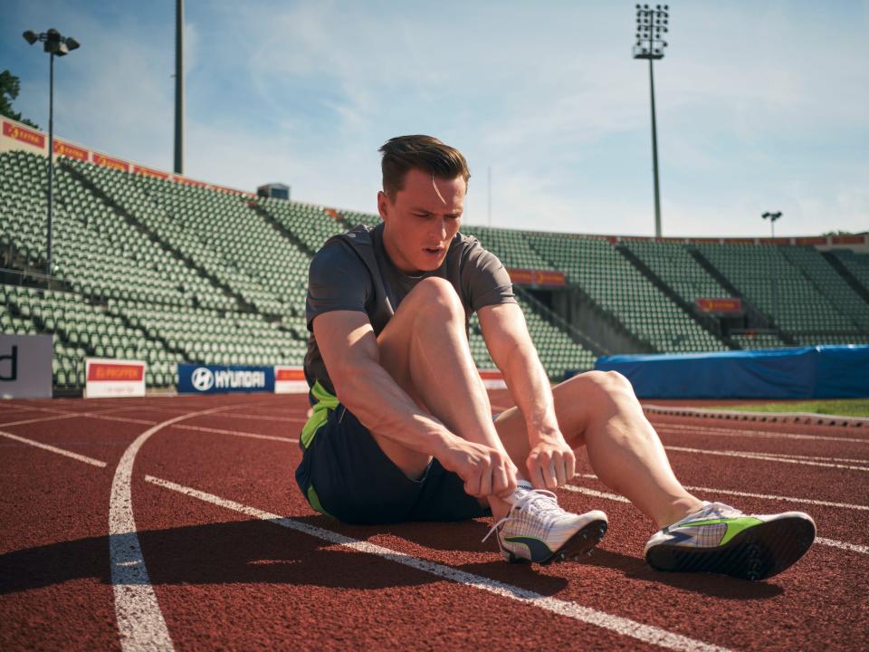 Karsten Warholm lacing up his trainers on a running track.