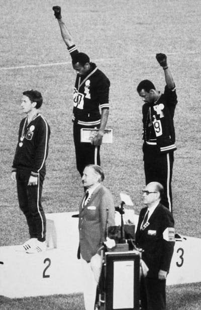 Two men in track suits at an awards ceremony raising their fists.