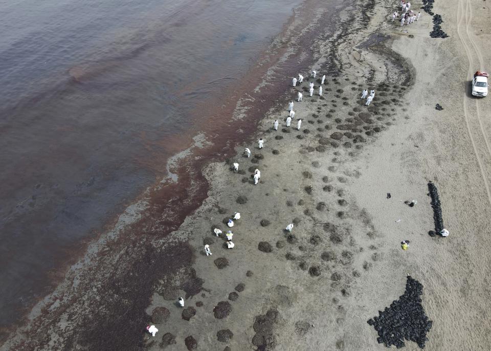 Workers, dressed in protective suits, continue to clean Conchitas Beach contaminated by an oil spill, in Ancon, Peru, Thursday, Jan. 20, 2022. The oil spill on the Peruvian coast was caused by the waves from an eruption of an undersea volcano in the South Pacific nation of Tonga. (AP Photo/Martin Mejia)