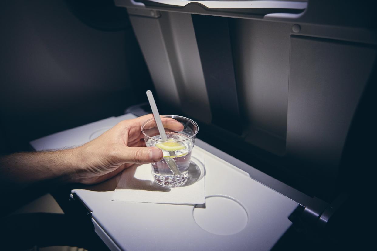 Traveling by airplane. Passenger enjoying gin and tonic drink in economy class during flight.
