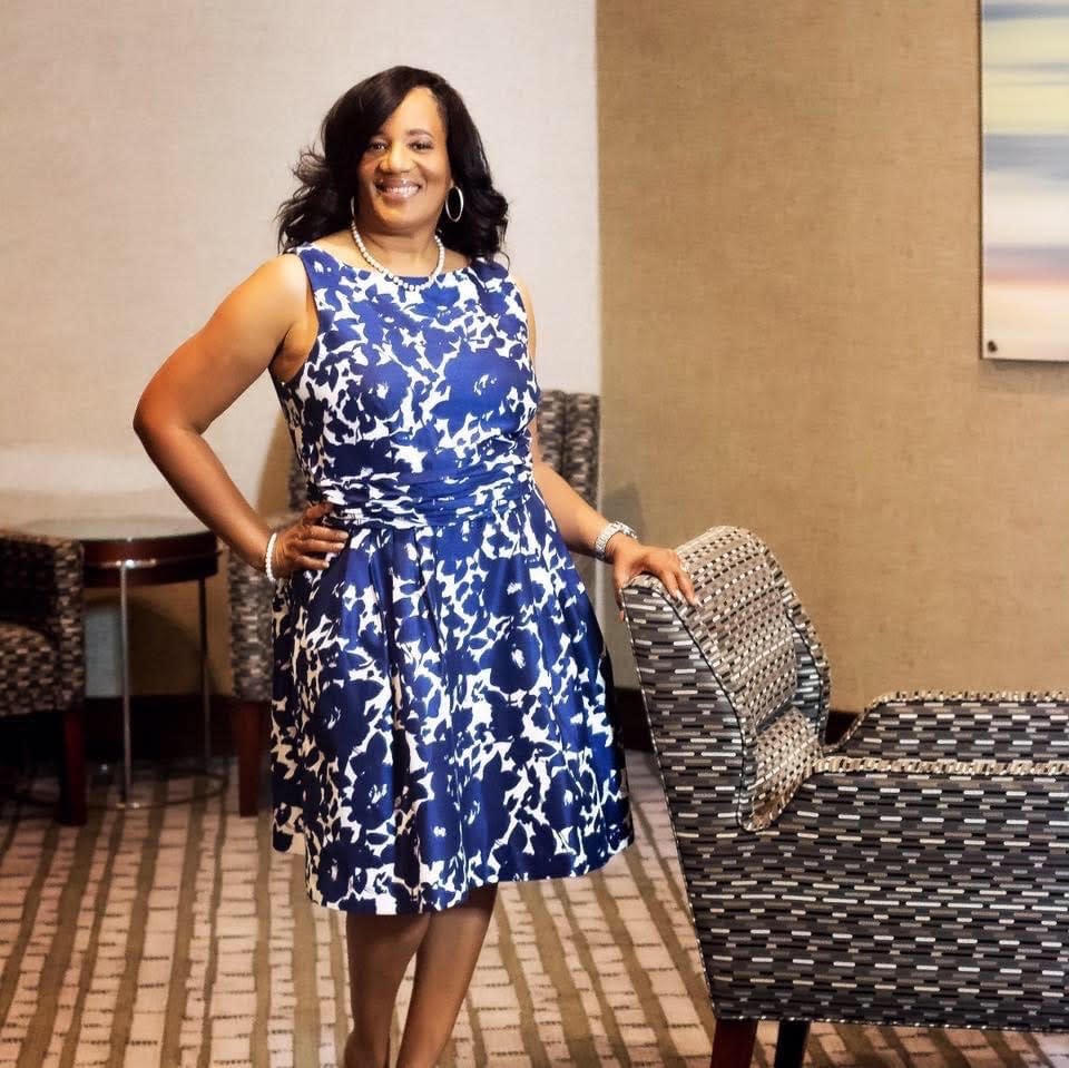 Tannie Coward stands in a blue floral dress in a professional setting