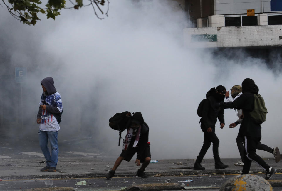 Protesters stand in clouds of tear gas launched by police to disperse them, in Quito, Ecuador, Friday, Oct. 4, 2019, during a nationwide transport strike that shut down taxi, bus and other services in response to a sudden rise in fuel prices. Ecuador's President Lenín Moreno, who earlier declared a state of emergency over the strike, vowed Friday that he wouldn't back down on the decision to end costly fuel subsidies, which doubled the price of diesel overnight and sharply raised gasoline prices. (AP Photo/Dolores Ochoa)