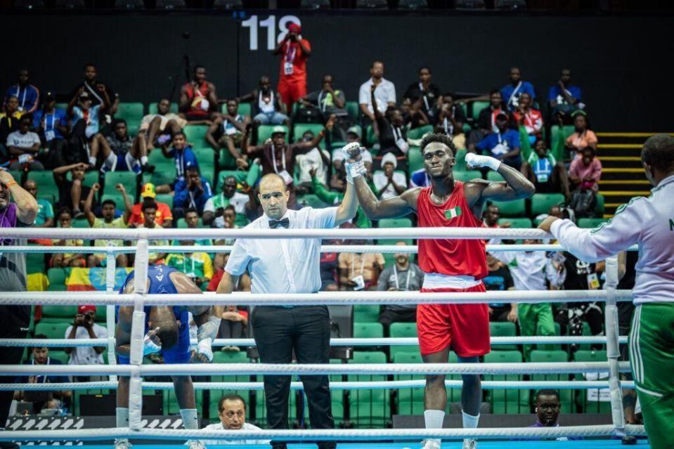 Adam Olaore, con el uniforme rojo y la bandera nigeriana en el pecho, recibe la mano en alto del árbitro mientras gana el Campeonato Africano de 2023