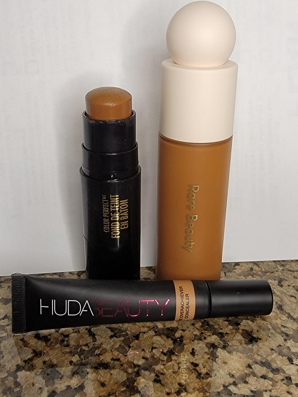 A Huda Beauty concealer, a foundation stick, and Rare Beauty foundation