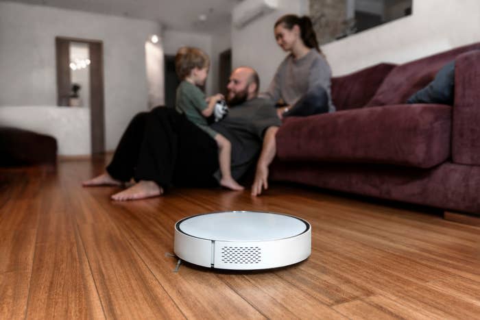 A family relaxes together in a living room while a robotic vacuum cleaner operates on the floor