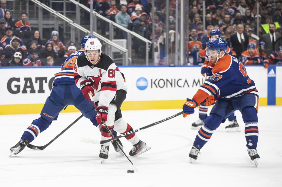 New Jersey Devils' Jack Hughes (86) gets past Edmonton Oilers' Mattias Ekholm (14) and Connor McDavid (97) during first-period NHL hockey game action in Edmonton, Alberta, Sunday, Dec. 10, 2023. (Jason Franson/The Canadian Press via AP)