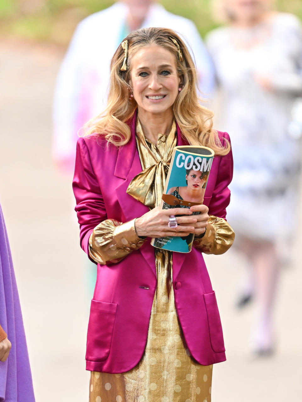 Sarah Jessica Parker on the set of 'And Just Like That', wearing a bright pink blazer and gold dress - her chin mole isn't visible