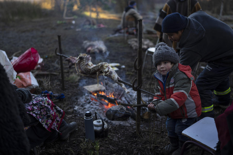 Gonzalo Rauque, 3, helps his mother, Constanza, rotate a rack of lamb during the multiday celebration of We Tripantu, the Mapuche new year, in the Corayen community of Los Rios, southern Chile, on Tuesday, June 21, 2022. (AP Photo/Rodrigo Abd)