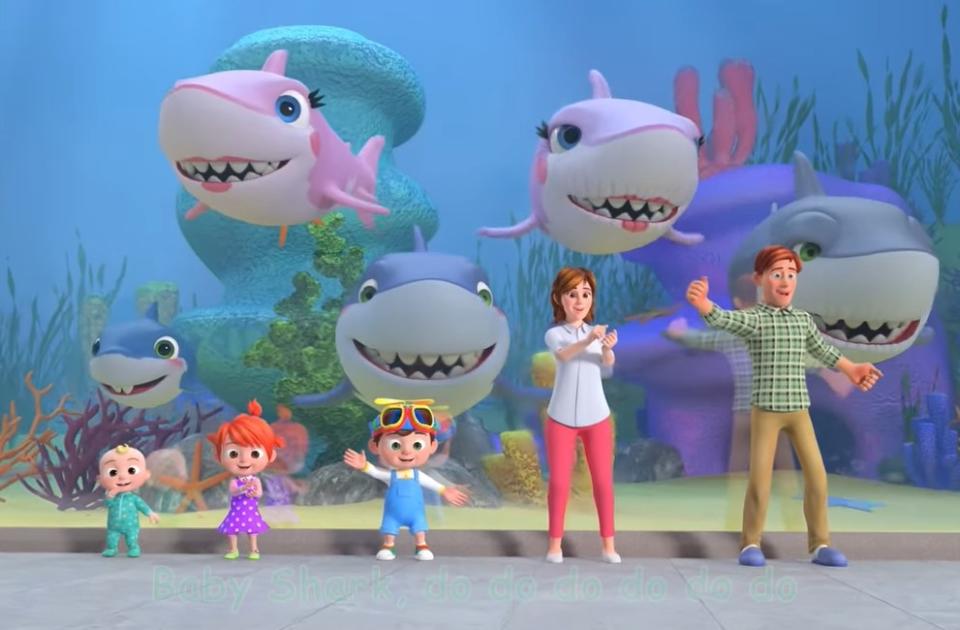 The Cocomelon family of JJ, Yoyo, Tom Tom, Mom, and Dad ready to dance with their sharks are behind them in an aquarium