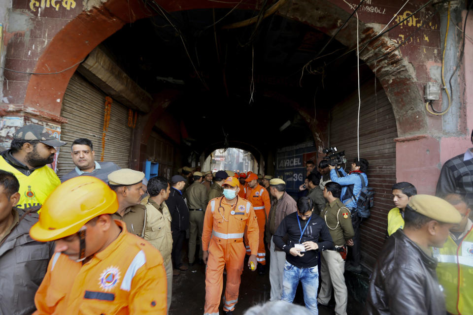 Medical officers and policemen walk near the site of a fire in an alleyway, tangled in electrical wire and too narrow for vehicles to access, in New Delhi, India, Sunday, Dec. 8, 2019. Dozens of people died on Sunday in a devastating fire at a building in a crowded grains market area in central New Delhi, police said. (AP Photo/Manish Swarup)