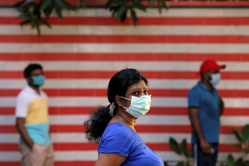 People wearing protective masks wait in a line to withdraw cash from a mobile ATM machine on a truck near a village during the curfew imposed by the government amid concerns about the spread of coronavirus disease, in Colombo