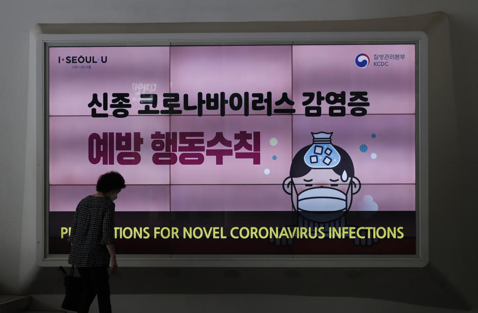 A woman wearing a face mask walks near a screen displaying precautions against the coronavirus in Seoul, South Korea, Friday, Aug. 14, 2020. South Korea reported over 100 new virus cases Friday, one of its biggest daily jumps in months, as officials express concerned that infections are getting out of control in cities as people increasingly venture out in public. (AP Photo/Lee Jin-man)