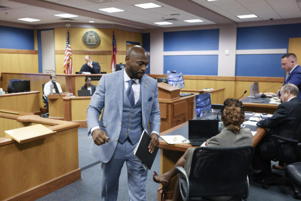 A man in a light blue suit walks past tables in a courtroom.