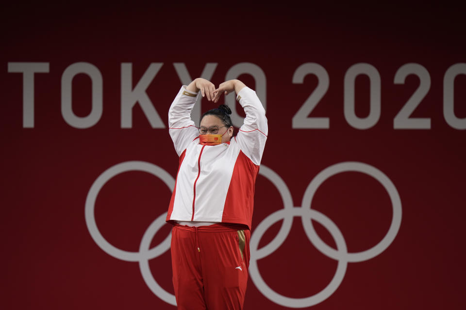 Li Wenwen of China makes a heart with her hands as she takes the podium to receive the gold medal in the women's +87kg weightlifting at the 2020 Summer Olympics, Monday, Aug. 2, 2021, in Tokyo, Japan. (AP Photo/Luca Bruno)