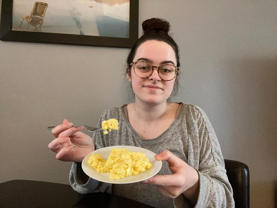 The writer sits at black table and eats scrambled eggs and holds fork