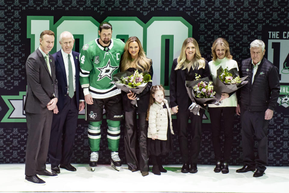 Dallas Stars left wing Jamie Benn (14) poses for a photo his family and Stars President Brad Alberts, left, general manager Jim Nill, second from left, prior to an NHL hockey game Saturday, March 4, 2023, in Dallas. Benn's fiancee Jessica Bennett, fourth from left, niece Sophia Benn, fourth from right, sister Jenny Benn, third from right, and parents Heather, second from right, and Randy Benn, right, also pose. (AP Photo/Emil T. Lippe)