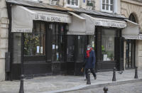 A woman wearing face a mask as a precaution against the coronavirus walks past a closed restaurant in Paris, Monday, Jan. 25, 2021. France's government may impose a third lockdown in the coming days if an existing 12-hour-a-day curfew doesn't significantly slow virus infections. (AP Photo/Michel Euler)