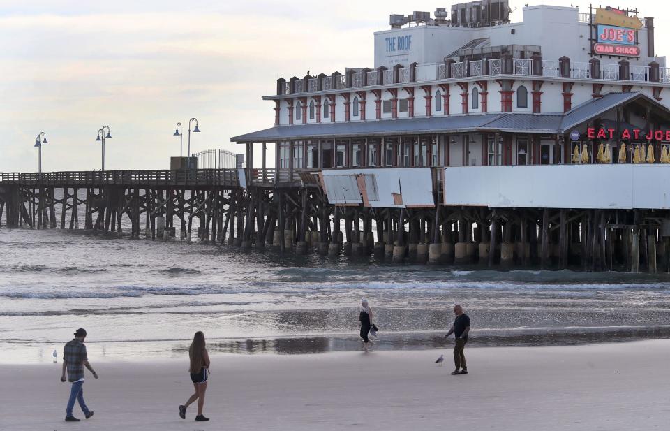 Morning beach walkers are pictured in early January strolling past the storm-damaged Daytona Beach Pier.