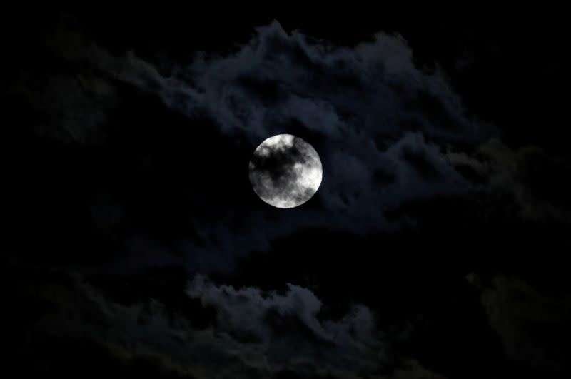 The full moon, also known as the Supermoon or Flower Moon, rises between clouds above Ronda