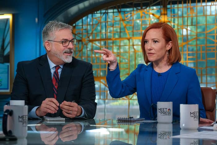 Jen Psaki wearing a blue blazer points while speaking to a male guest in a suit and tie on the "Meet the Press" set