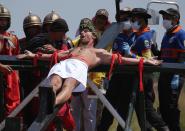 Danish national Lasse Spang Olsen, a 48-year-old filmmaker, grimaces as he is nailed to a cross to re-enact the crucifixion of Jesus Christ in San Juan village, Pampanga province, northern Philippines on Friday, April 18, 2014. Church leaders and health officials have spoken against the practice which mixes Roman Catholic devotion with folk belief, but the annual rites continue to draw participants and huge crowds. (AP Photo/Aaron Favila)