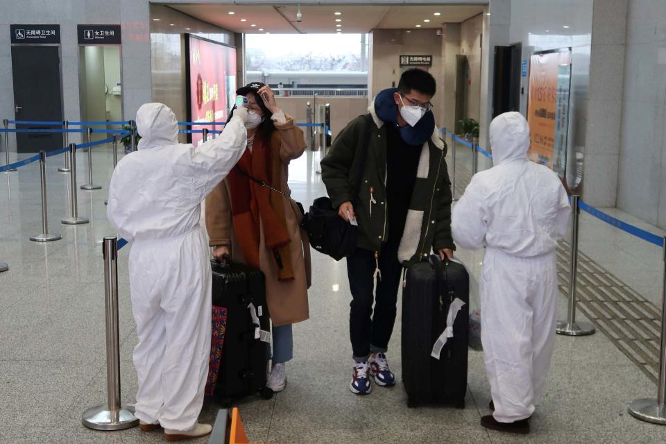 Workers in protective suits check the temperature of passengers arriving at the Xianning North Station (REUTERS)