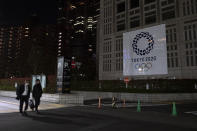 Two men walk past a large banner promoting the Tokyo 2020 Olympics in Tokyo, Tuesday, March 24, 2020. IOC President Thomas Bach has agreed "100%" to a proposal of postponing the Tokyo Olympics for about one year until 2021 because of the coronavirus outbreak, Japanese Prime Minister Shinzo Abe said Tuesday. (AP Photo/Jae C. Hong)
