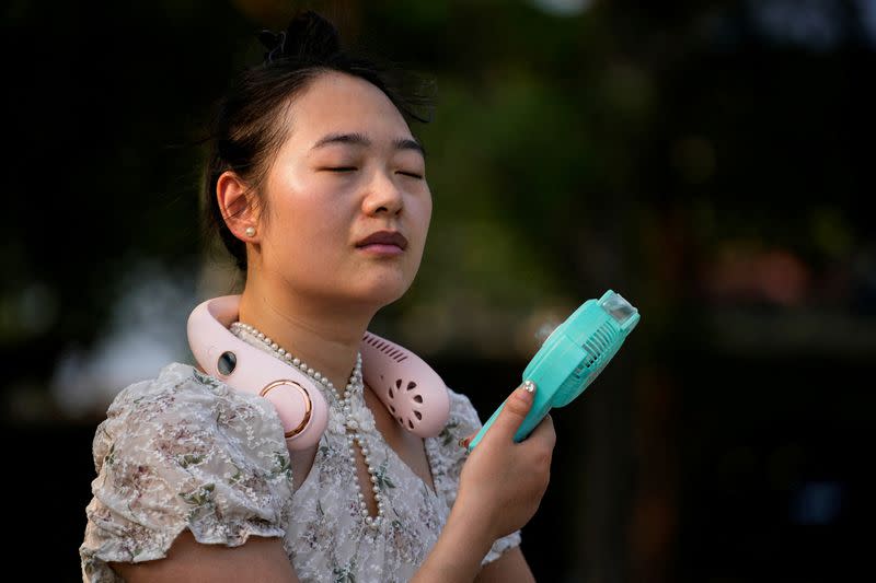 FILE PHOTO: A woman uses a fan as she walks at a park amid an alert for heatwave in Shanghai