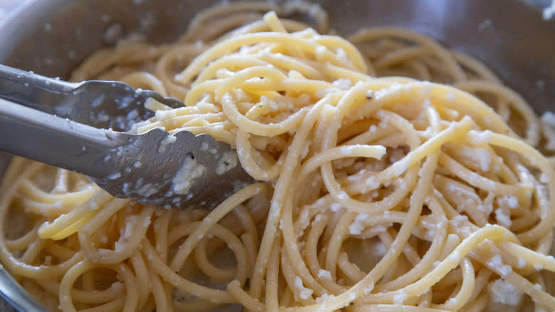 Closeup of tongs mixing cacio e pepe pasta