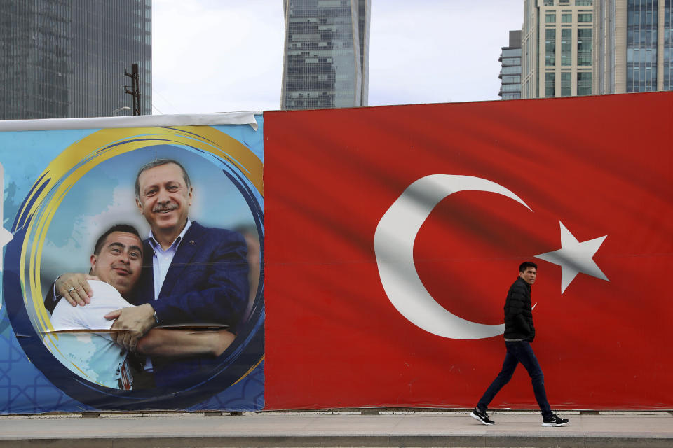 A man walks by a Turkish flag and a poster showing the Turkey's President Recep Tayyip Erdogan with a boy in Ankara, Turkey, Sunday, March 31, 2019. Turkish citizens have begun casting votes in municipal elections for mayors, local assembly representatives and neighborhood or village administrators that are seen as a barometer of Erdogan's popularity amid a sharp economic downturn. (AP Photo/Ali Unal)