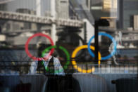 The Olympics rings are reflected on the window of a hotel restaurant as a server with a mask sets up a table Monday, Feb. 24, 2020, in the Odaiba section of Tokyo. (AP Photo/Jae C. Hong)